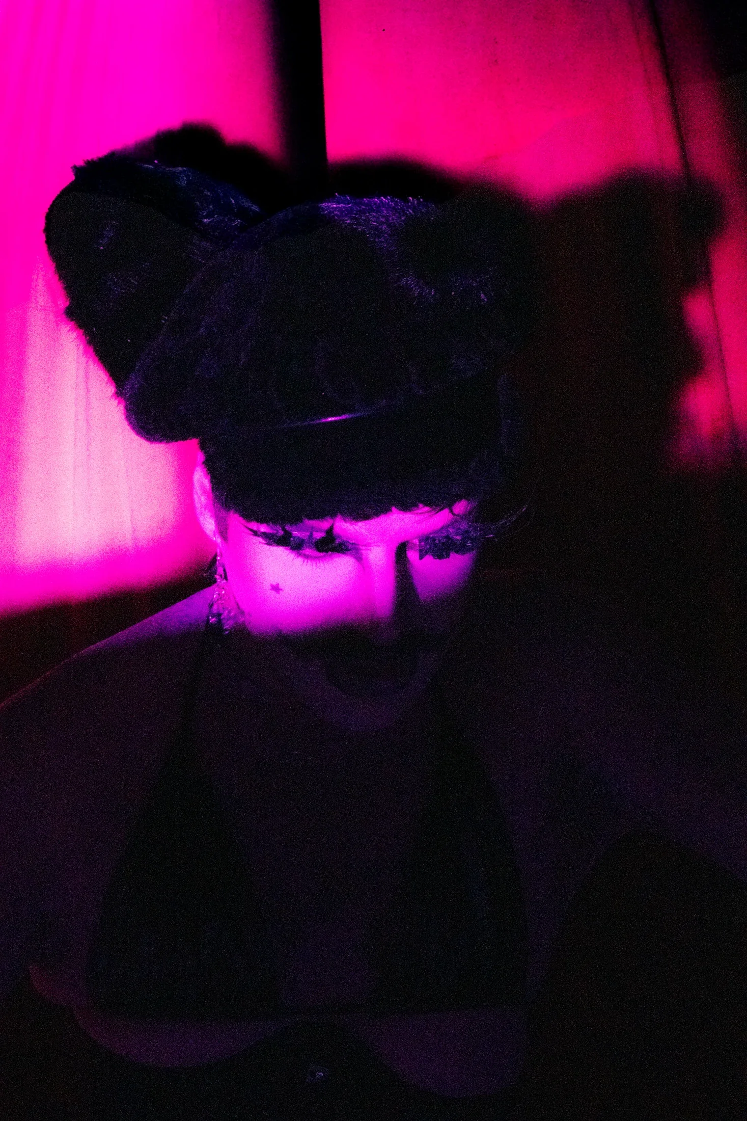 A narrow wash of pink light reveals a performer’s eyes beneath a black textured cap.