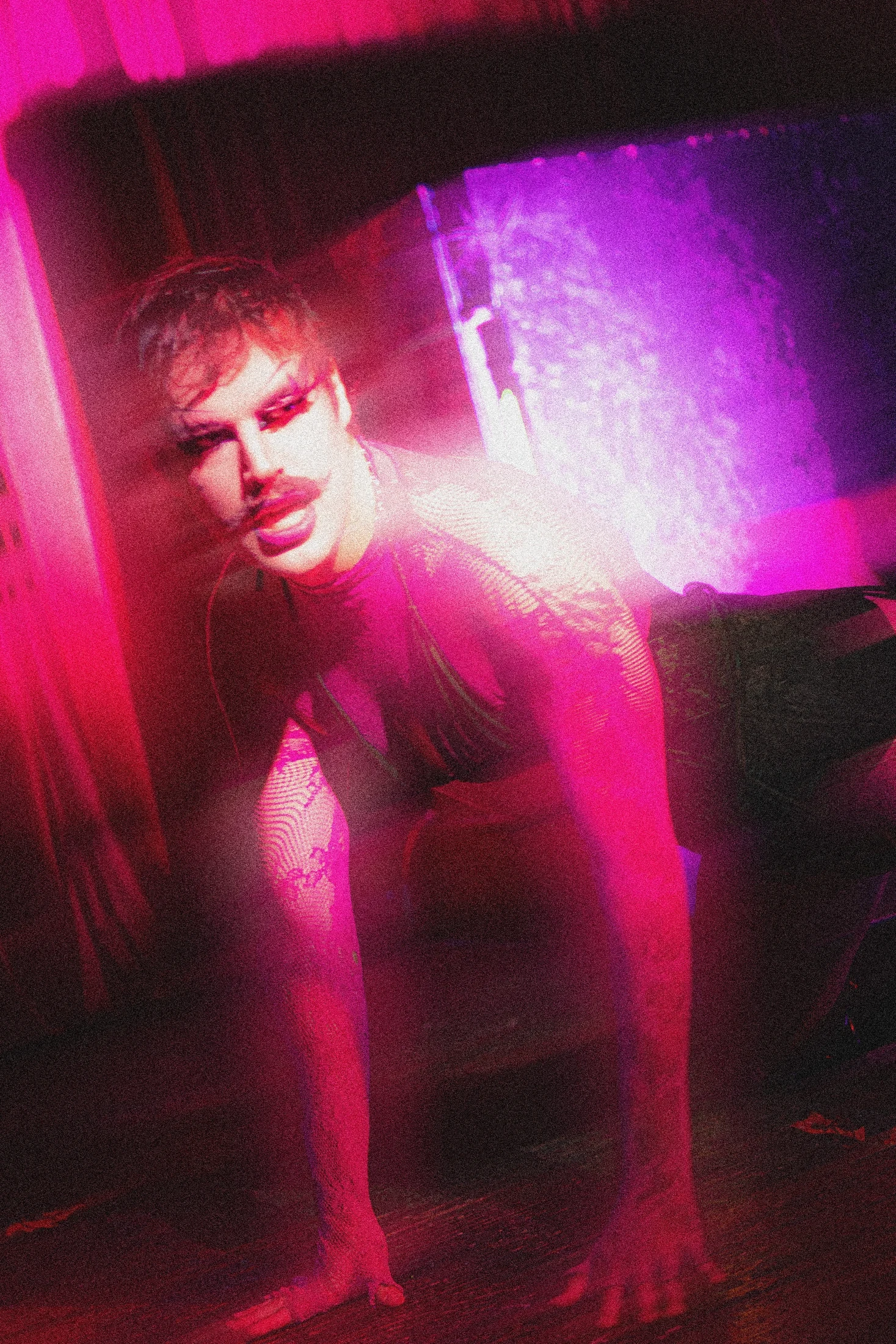 A performer leans toward the camera through pink and purple light trails.