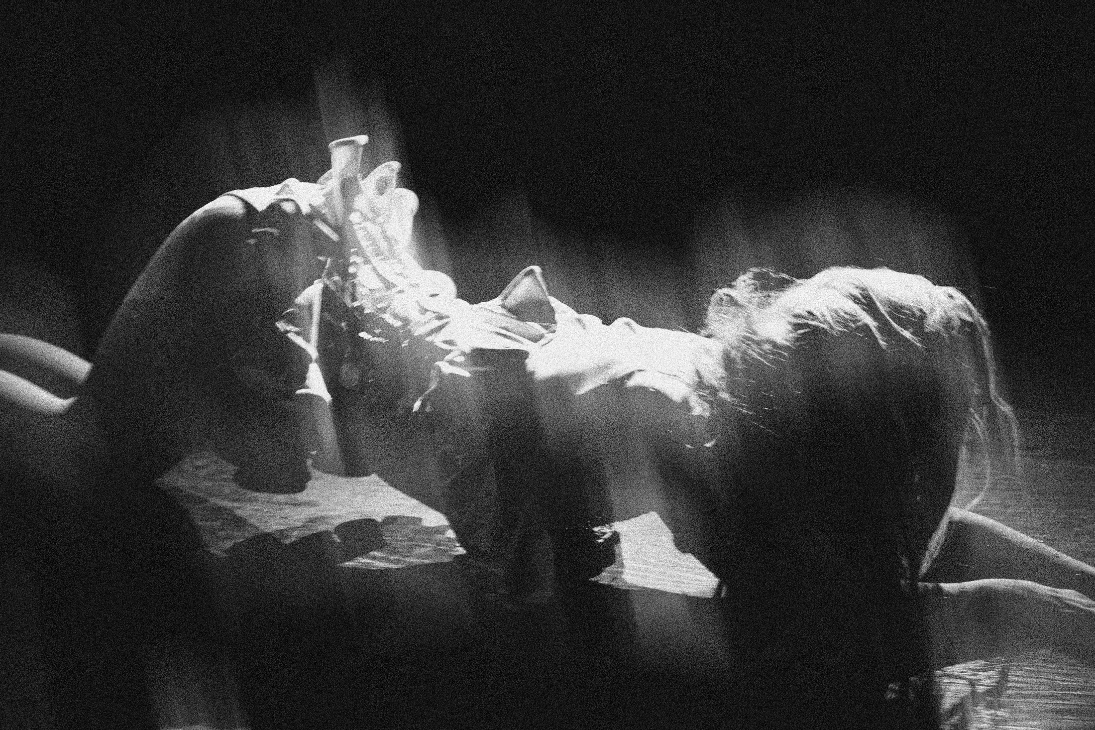 Black-and-white photograph of a performer arching back on the stage floor in a shaft of light.